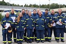 Gruppenbild aus 12 Anwärterinnen und Anwärter in Einsatzkleidung und Urkunden unter freiem Himmel